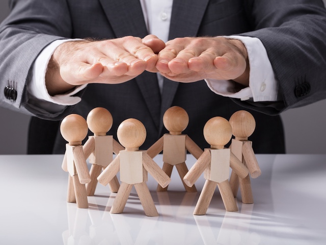 Human Hand Protecting Wooden Figures On White Background Human Hand Protecting Wooden Figures On White Background